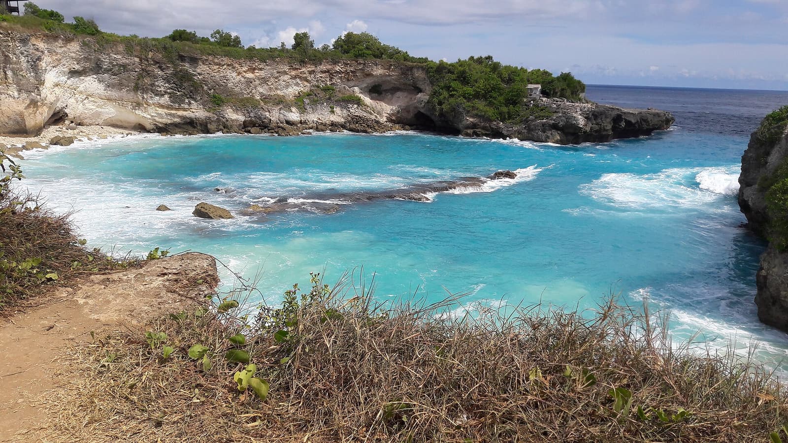 The bright blue water of the Blue Lagoon beneath limestone cliffs on Nusa Ceningan
