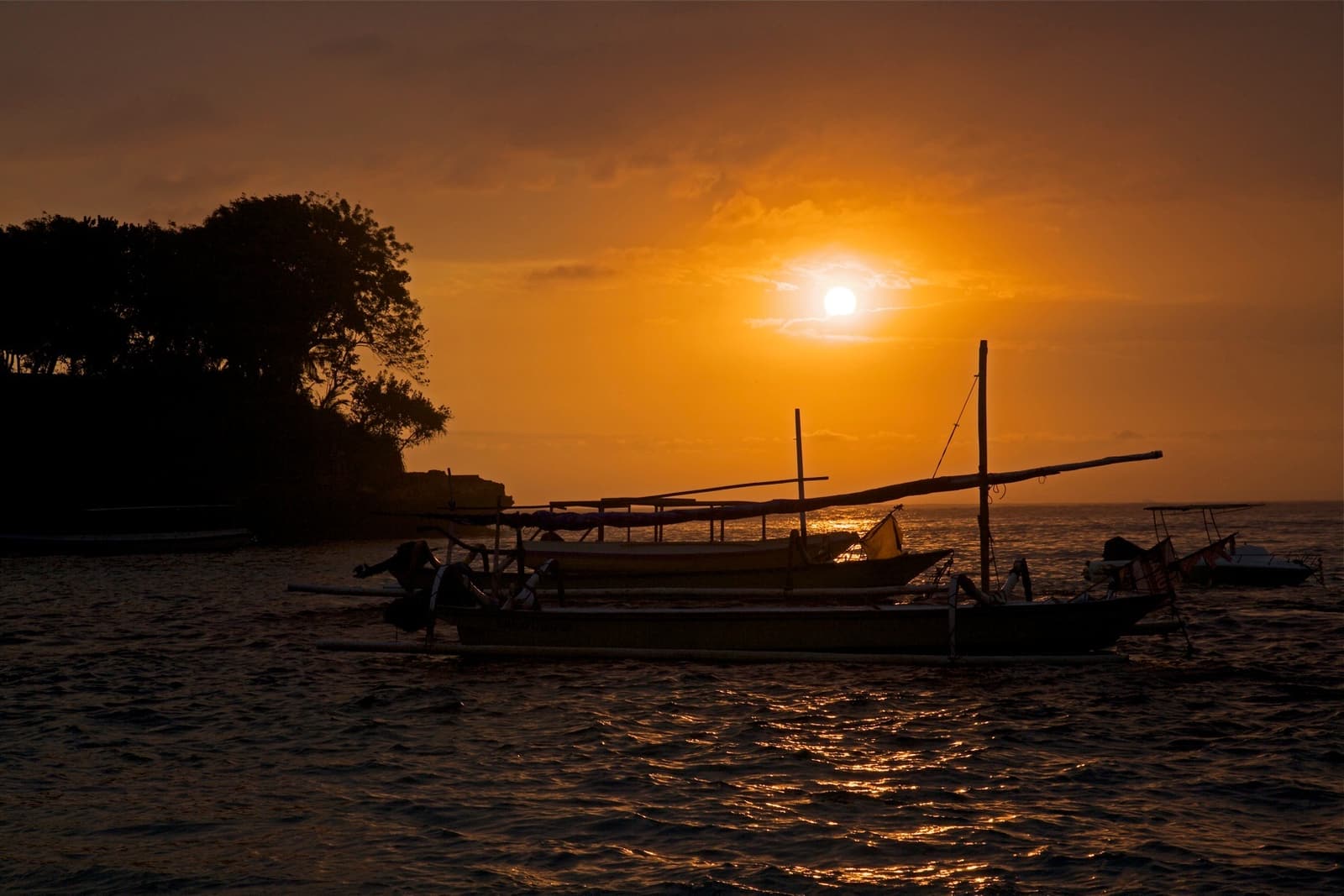 The sun setting over the sea behind a boat at Nusa Lembongan